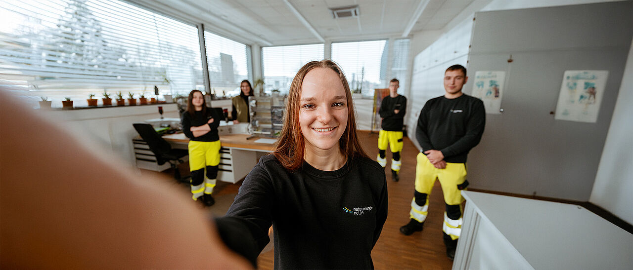 Teamaufnahme im technischen Arbeitsumfeld Mehrere Personen stehen in einem Technikraum mit Werkbänken und technischen Geräten.