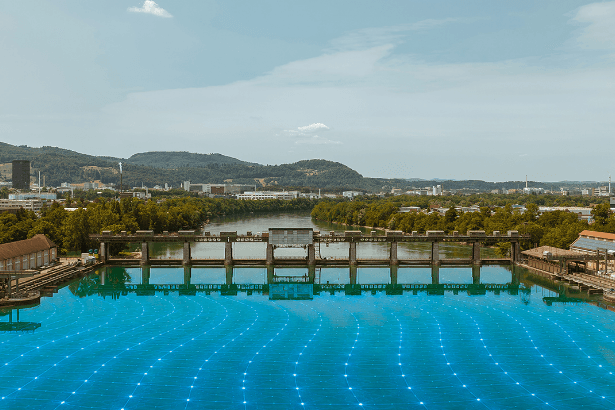 Wasserkraftwerk mit digitalem Energienetz Blick auf ein Wasserkraftwerk mit Stauwehr und blau visualisiertem Energienetz auf der Wasseroberfläche.