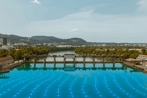 Wasserkraftwerk mit digitalem Energienetz Blick auf ein Wasserkraftwerk mit Stauwehr und blau visualisiertem Energienetz auf der Wasseroberfläche.
