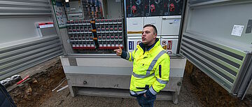 Person erklärt Technik an offener Trafostation im neuen Wohngebiet