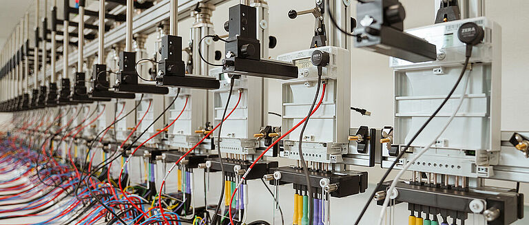 Reihe automatisierter Stromzähler mit mechanischen Armen und Kabeln – verwendet zur Prüfung oder Probenverarbeitung in technischer Umgebung.
