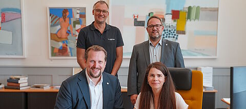 4 Personen stehend und am Tisch 