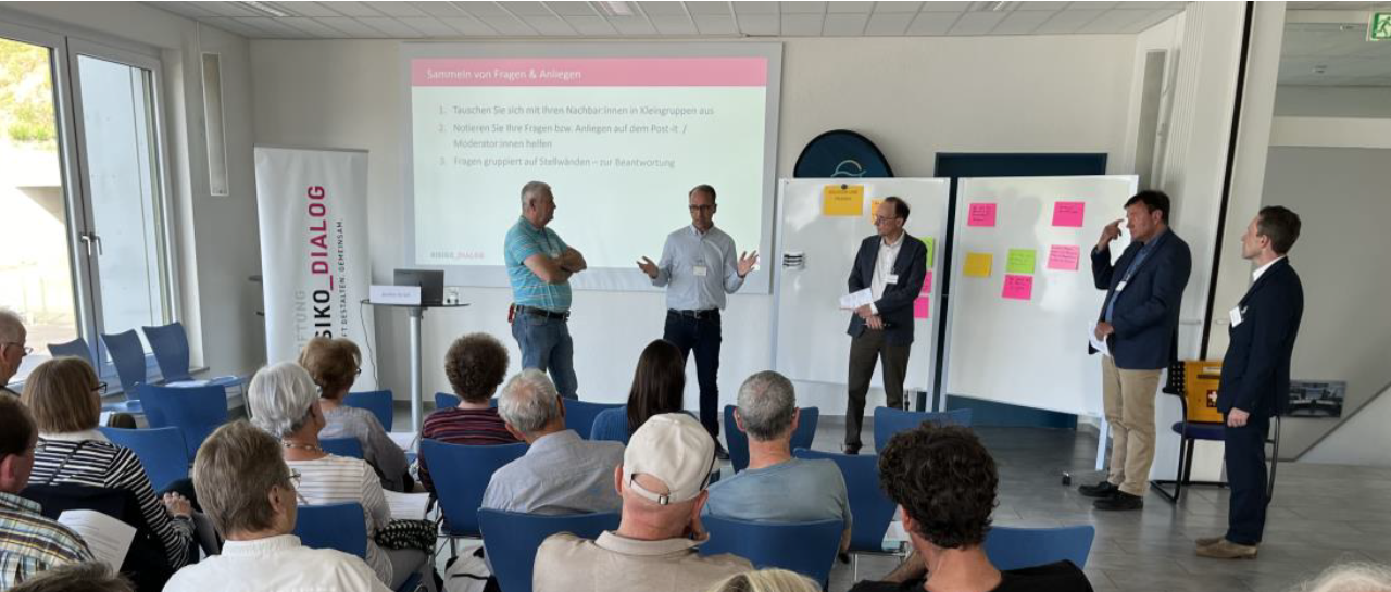 Diskussion und Präsentation in einem Seminarraum Eine Gruppe von Menschen nimmt an einer Präsentation in einem Seminarraum teil; vier Männer stehen vorne und sprechen zu den sitzenden Teilnehmern.